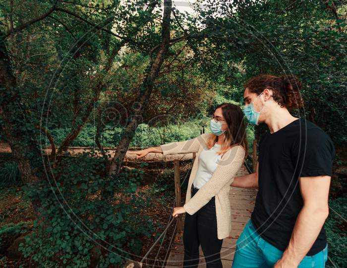Young Woman Pointing Out Something To His Partner In The Forest With The Masks On