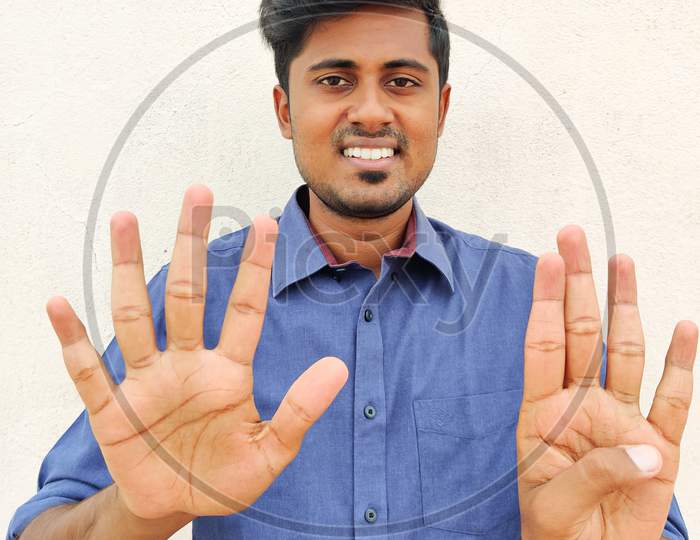 Smiling South Indian Young Man Wearing Blue Shirt Pointing Up With Fingers Number Nine. Isolated On White Background.