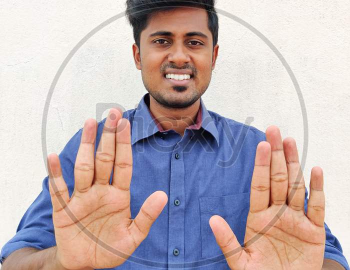 Smiling South Indian Young Man Wearing Blue Shirt Pointing Up With Fingers Number Ten. Isolated On White Background.