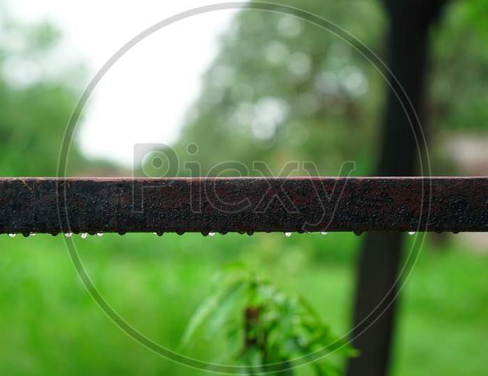 Selective focus on old rectangular iron pipe with rainy water drops. Rough old pipe with blurred background.