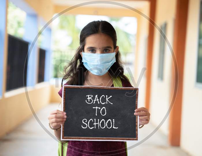 Young Girl In Medical Mask Holding Back To School Signage Board At Corridor - Concept Of School Reopen, Lifestyle And New Normal.