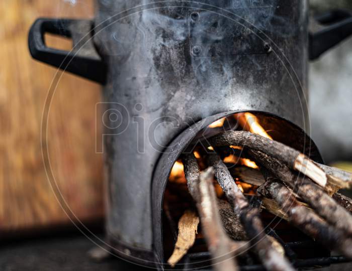 Pressure Cooker Kept On Top Of A Modern Chulah With Wood Being Burnt.