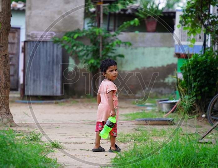 Little Indian kid with the bottle walking in the farmland.