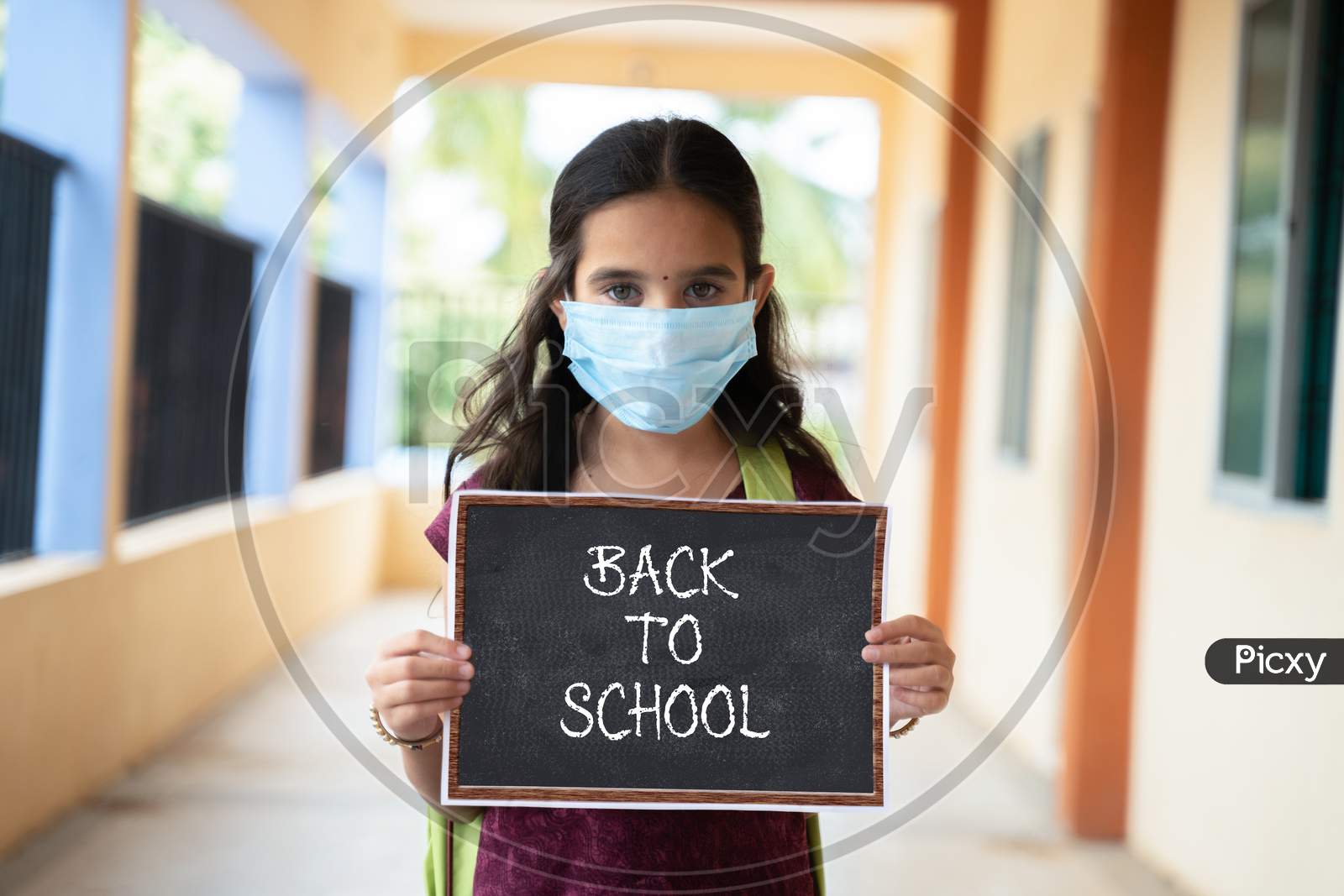 Young Girl In Medical Mask Holding Back To School Signage Board At Corridor - Concept Of School Reopen, Lifestyle And New Normal.