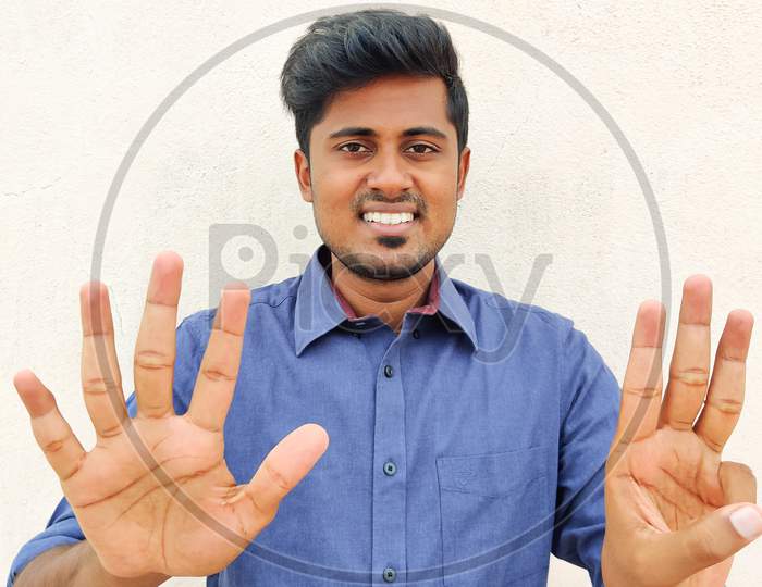 Smiling South Indian Young Man Wearing Blue Shirt Pointing Up With Fingers Number Eight. Isolated On White Background.