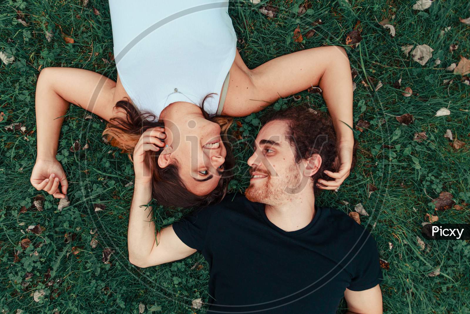Young Couple Smiling Each Other While Lying On The Grass