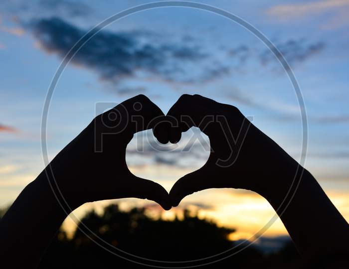 Silhouette hand in heart shape with sunset, Valentine's day concept.