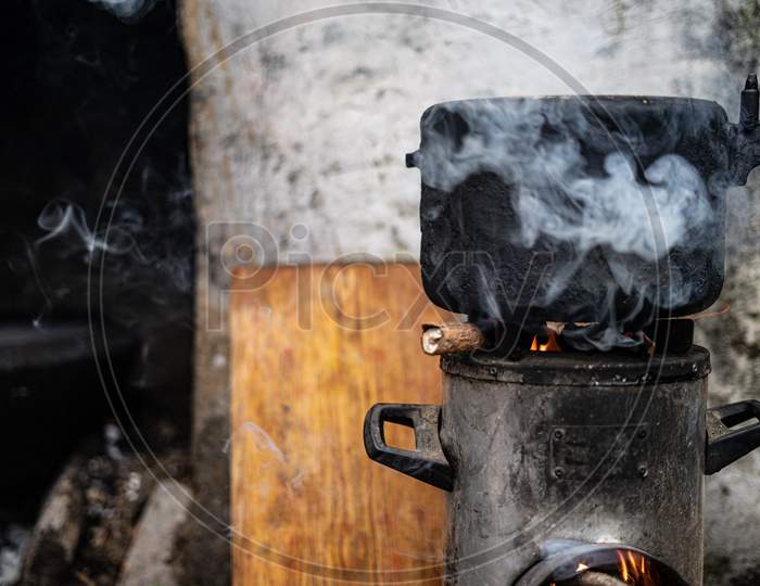 Pressure Cooker Kept On Top Of A Modern Chulah With Wood Being Burnt.