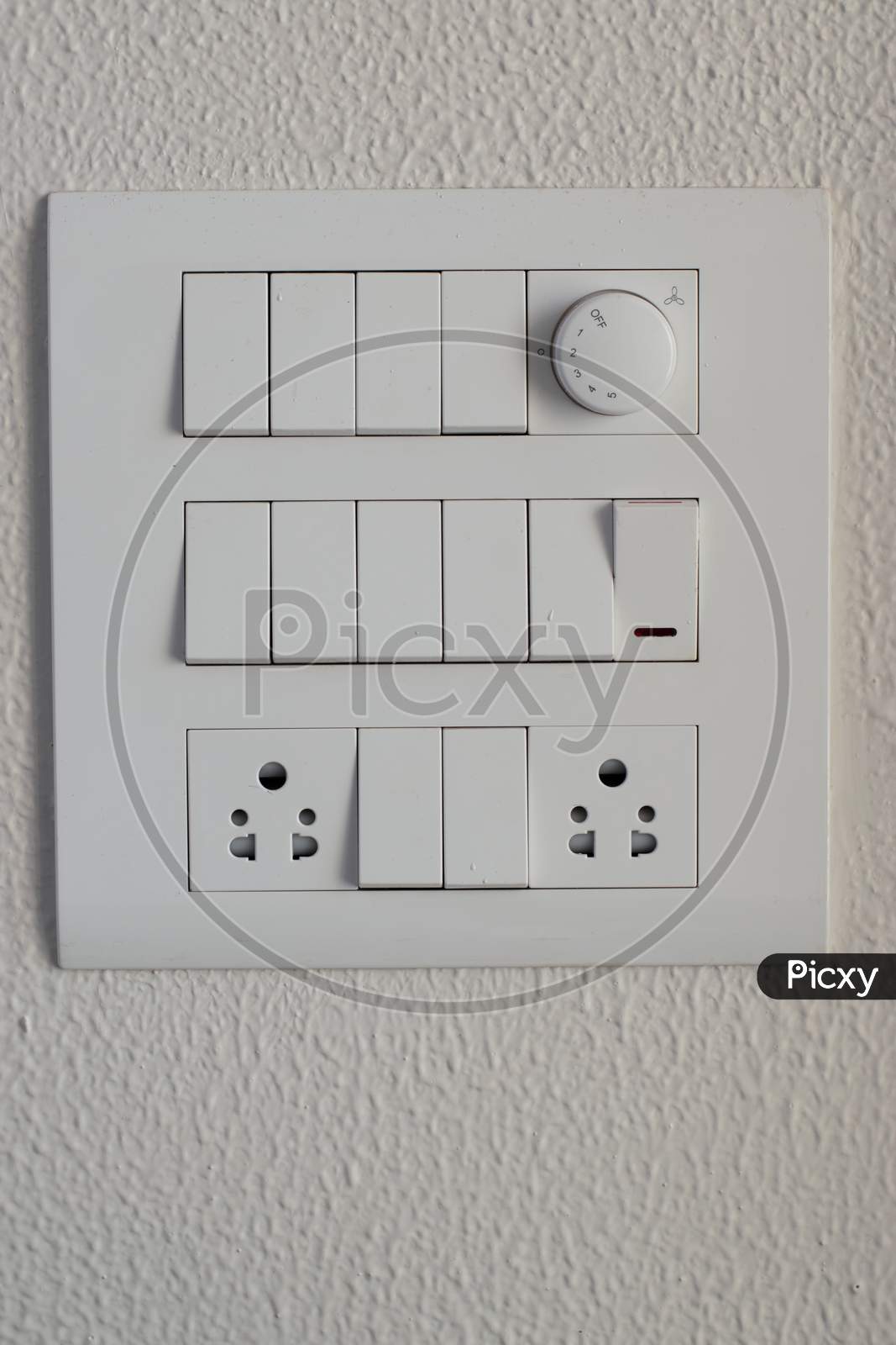 Designer Electrical White Switch Board With Regulator And Switches And Three Pin Sockets On The White Wall