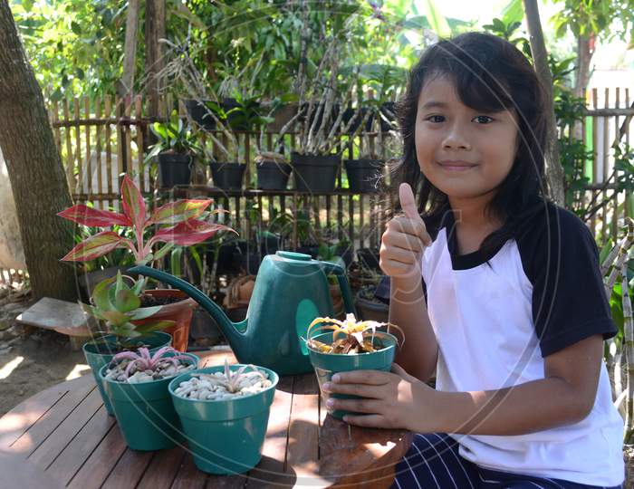 Beautiful Little Girl Smile With Thumbs Up When Sit Holding Plant In Pots Look To Camera