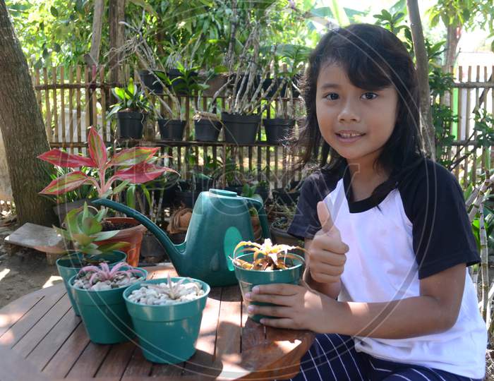 Little Girl Toothy With Thumbs Up When Sit Holding Plant In Pots