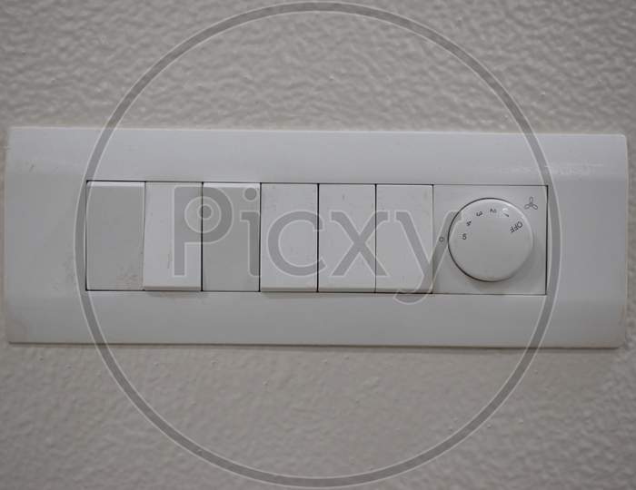 Designer Electrical White Switch Board With Regulator And Six Switch On The White Wall