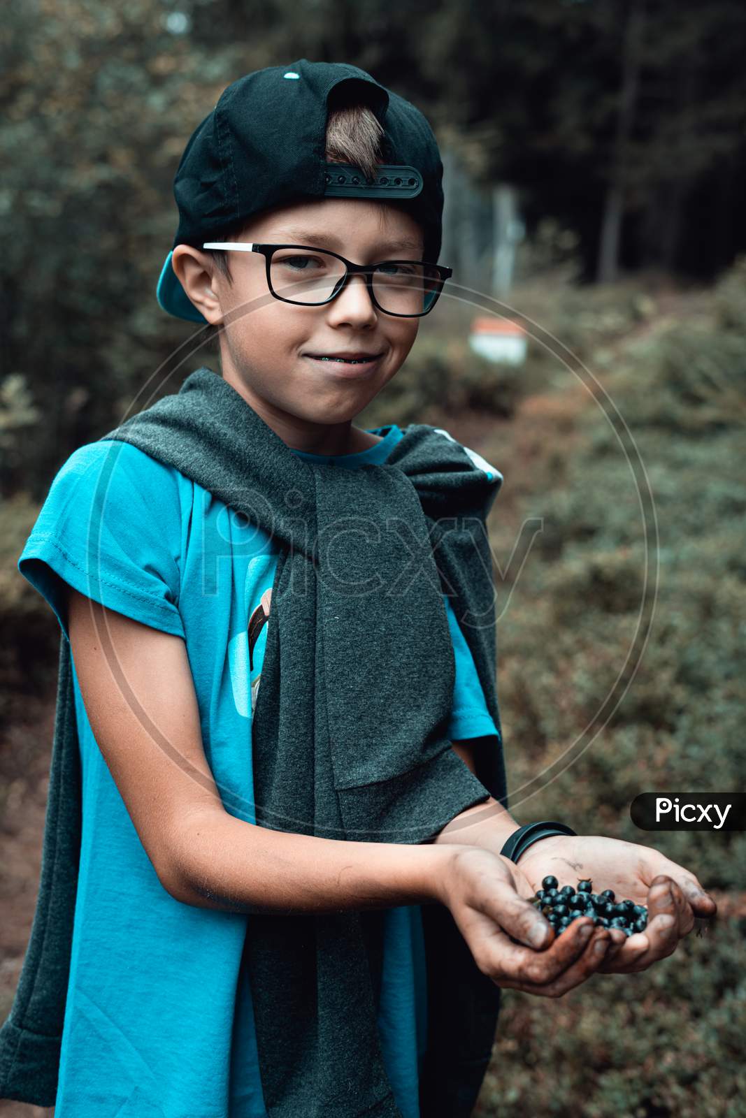 boy standing in the forest with hands full of blueberries.