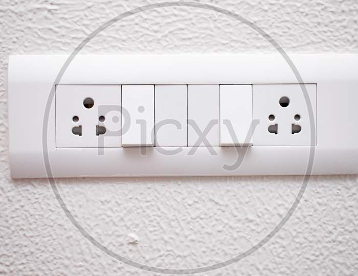 Designer Electrical White Switch Board With 3 Pin Socket And Two Switch On The White Wall