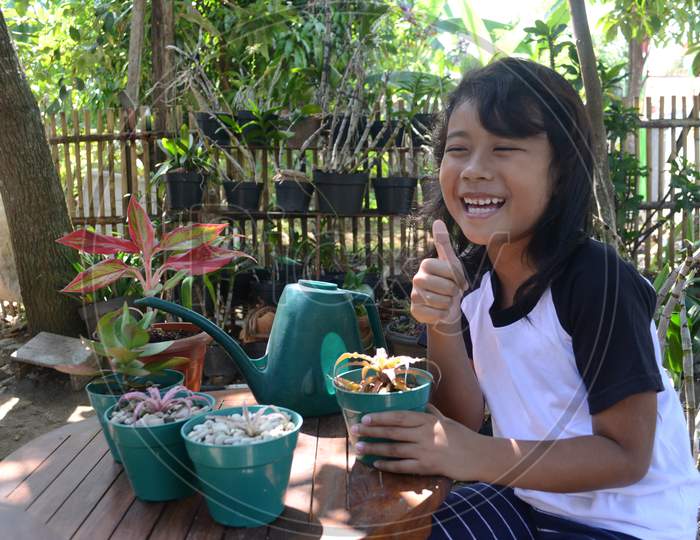 Asian Little Girl Laugh With Thumbs Up When Sit Holding Plant In Pots