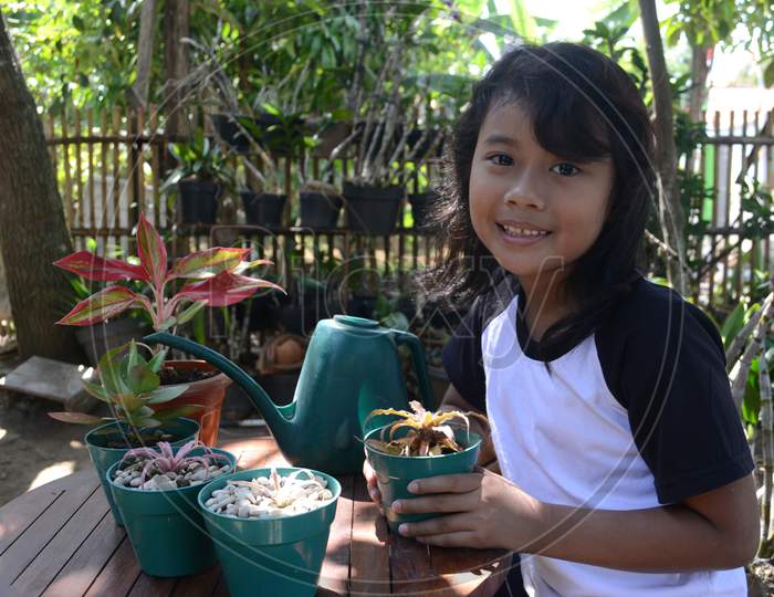 Little Girl Smile When Sit Holding Plant In Pots Look To Camera