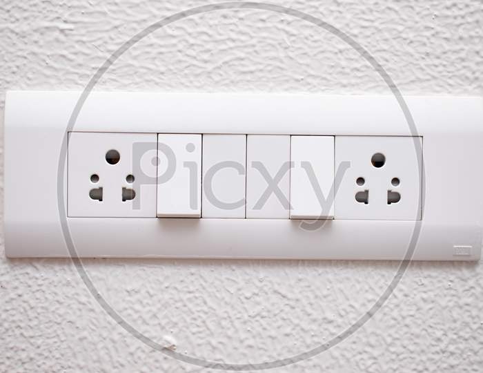Designer Electrical Switch Board With 3 Pin Socket And Two Switch On The White Wall