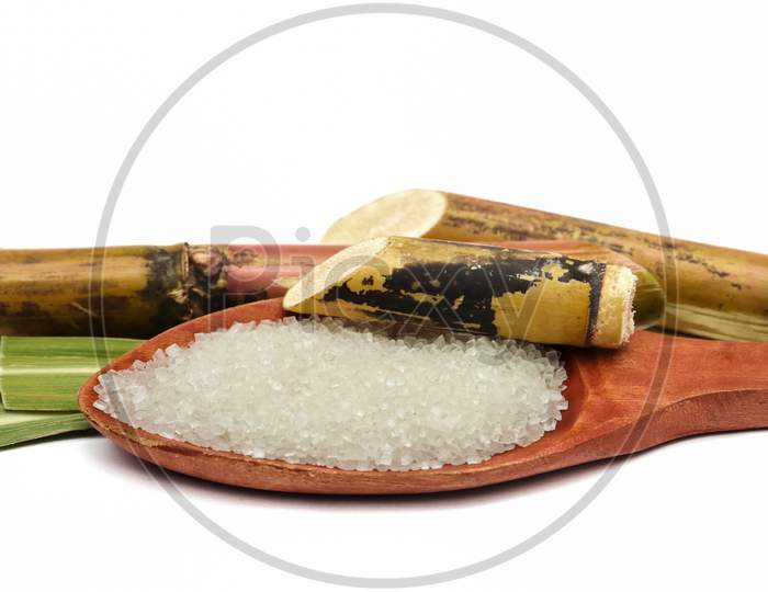 Closeup Of Sugar In A Wooden Ladle With Sugarcane Pieces In White Background