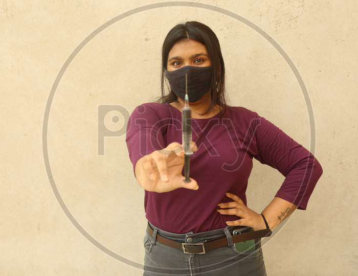 Young Indian Beautiful Girl Holding Blood Sample Filled Syringe Looking To The Camera Wearing A Protective Face Mask Against Wall Background, Close Up View