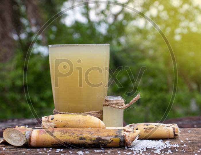 Sugarcane Juice In Glass with Sugar Cane Pieces On Wooden Surface With Selective Focus