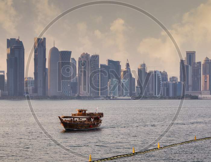 Doha skyline from the corniche promenade sunset shot showing dhow with Qatar flag in the Arabic gulf