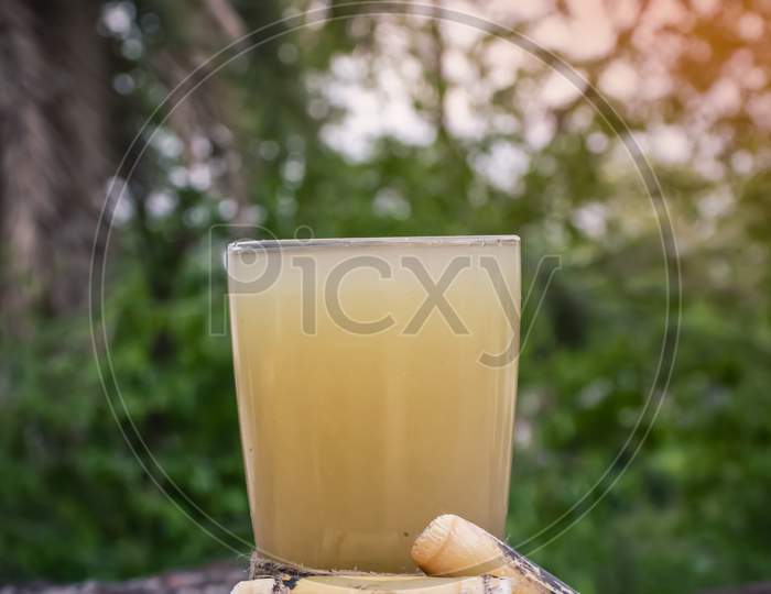 Sugarcane Juice In Glass with  Sugar Cane Pieces On Wooden Surface