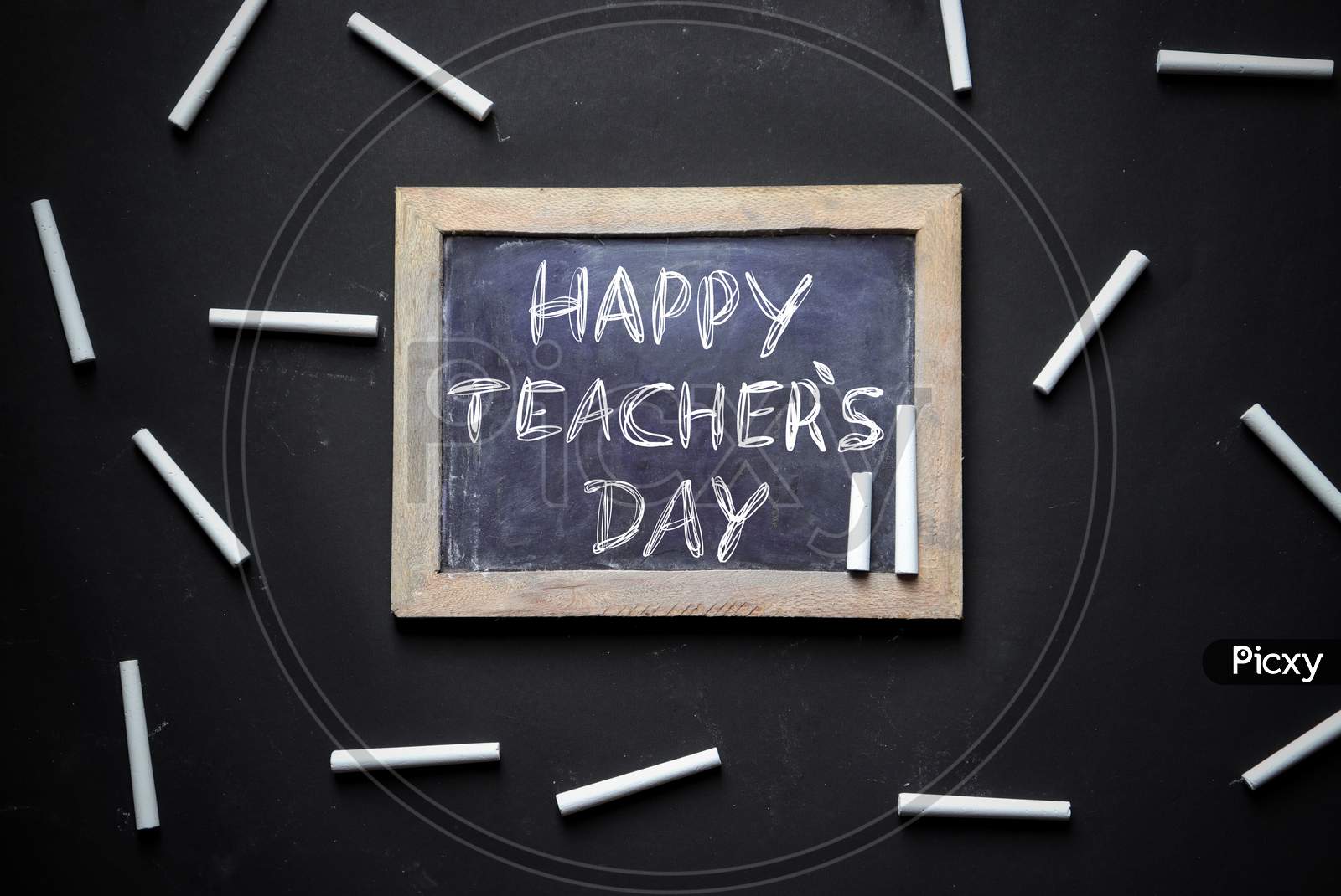 Happy Teacher's Day Written On Slate Board With White Chalk Pieces Isolated On Black Background, Perfect For Wallpaper