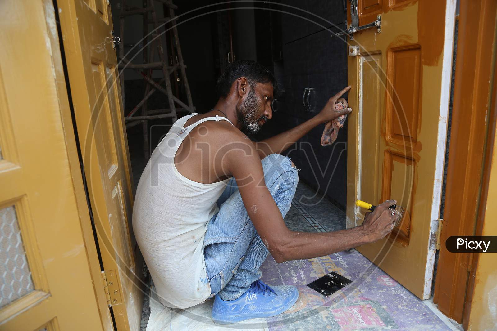 Jodhpur, Rajasthan, India, 20Th September 2020: Indian Male Adult Painting The Entrance Door Wearing Jeans And Vest While Sitting On The Floor Indoor Image, Indian Painters Furnishing Homes In Lock Down