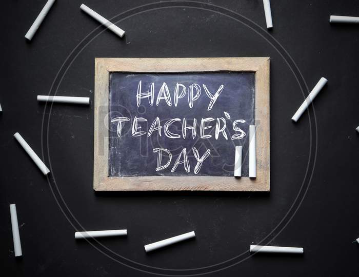 Happy Teacher's Day Written On Slate Board With White Chalk Pieces Isolated On Black Background, Perfect For Wallpaper