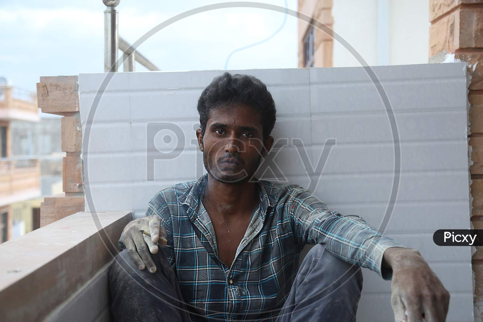 Jodhpur, Rajasthan, India, 20Th September 2020: Young Indian Male Labour Worker Smoking Cigarette Wearing Dirty Clothes While Sit Relaxing Against The White Wall At Workplace Taking Smoke Break.