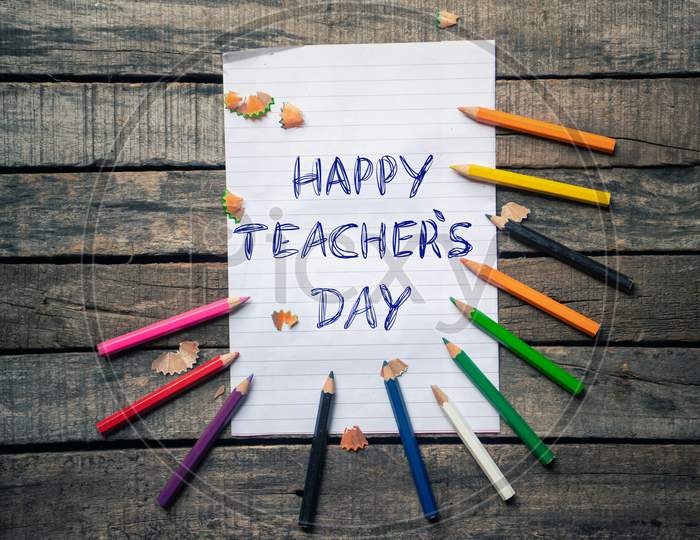 Happy Teacher's Day Wish Written Ruled Paper With Color Pencils On Wooden Background