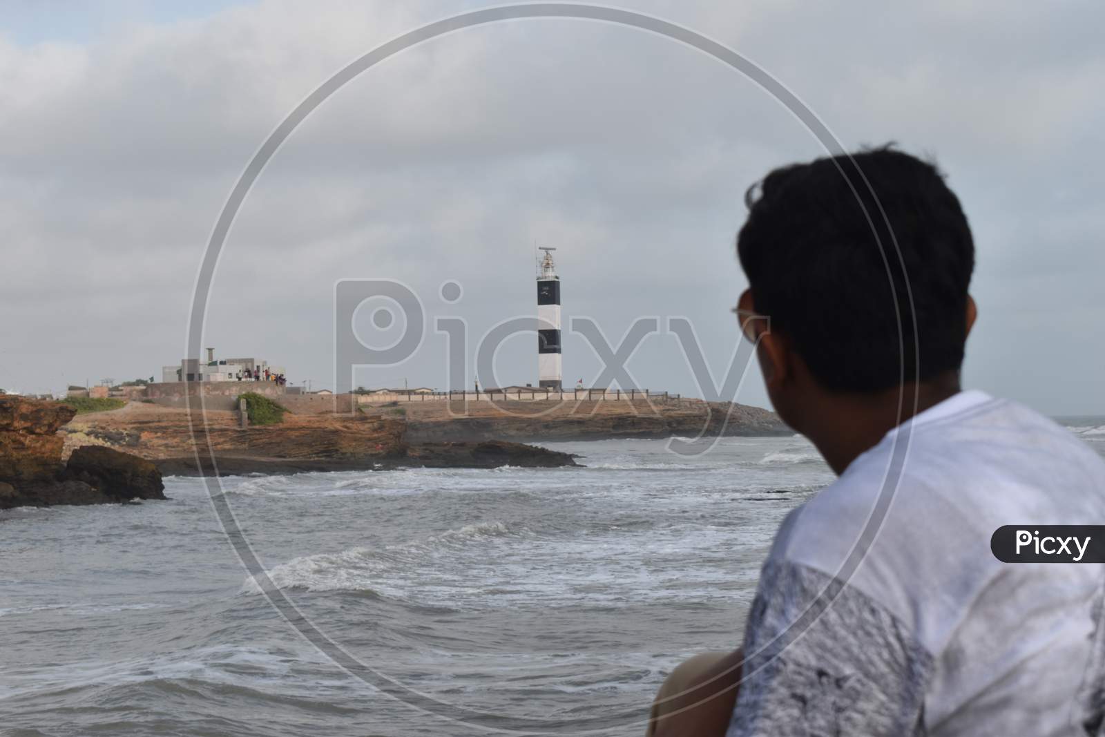 A boy watching the lighthouse at the shore of the sea