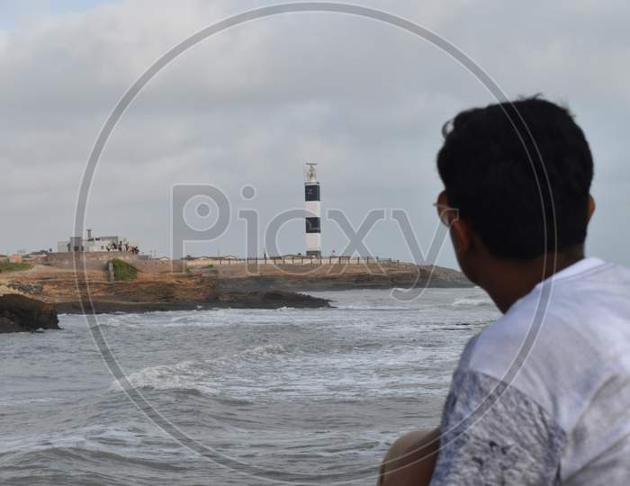 A boy watching the lighthouse at the shore of the sea