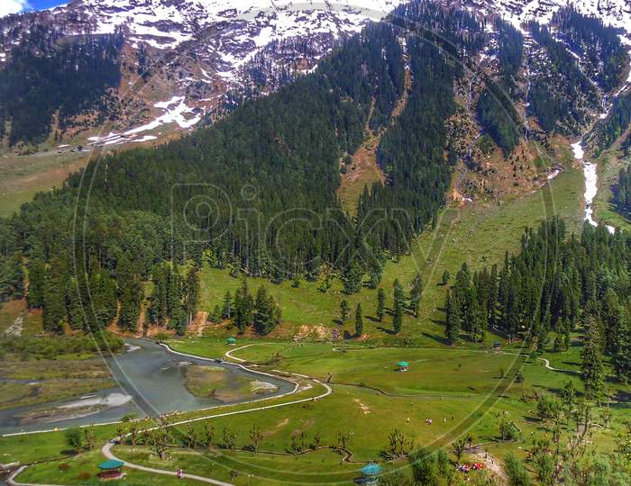 Lush green valley in Kashmir with himalayan river flowing along it and snowy mountains in the background