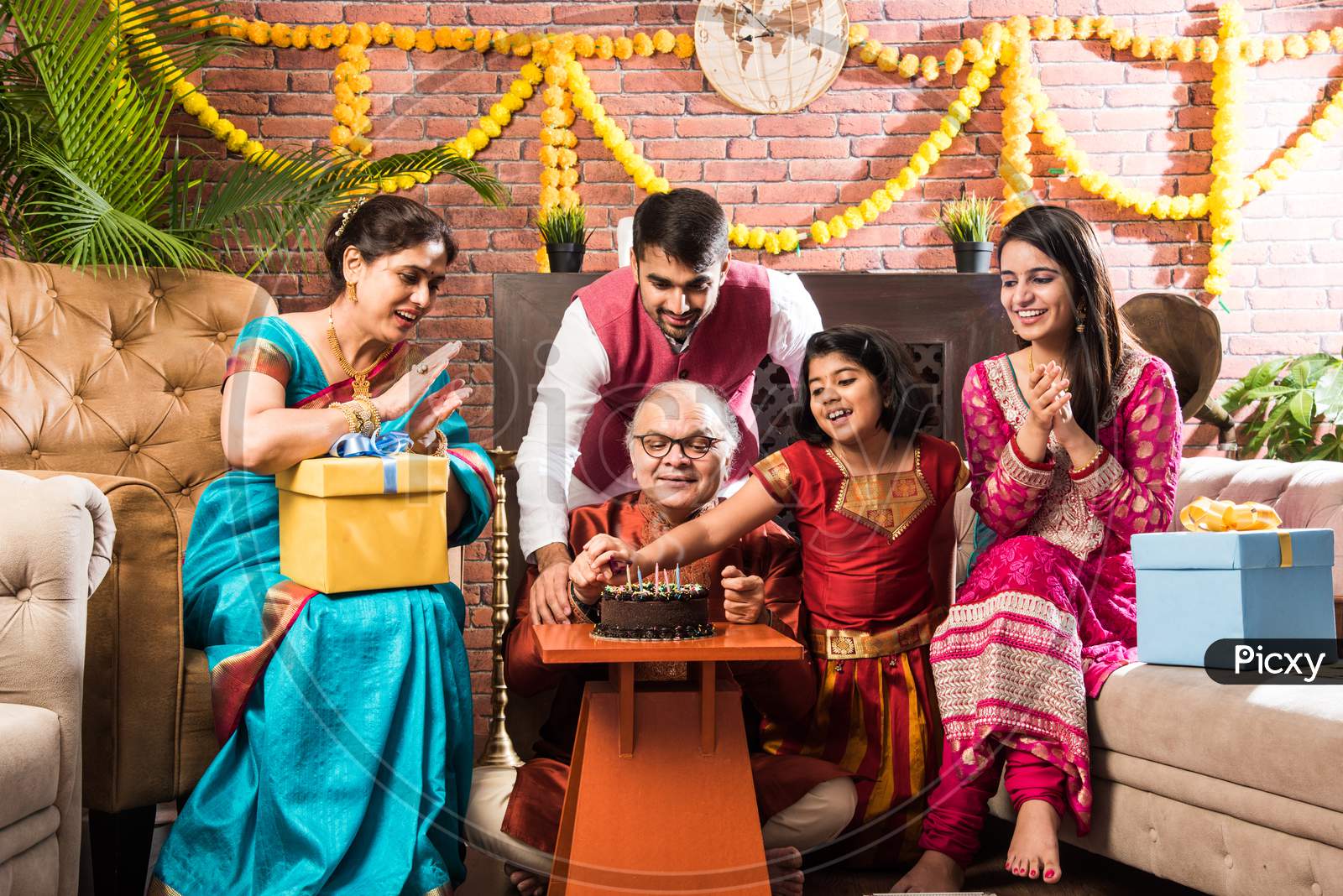 Senior Indian Asian Man Celebrating Birthday With Wife, Son, Daughter In Law And Grand Daughter