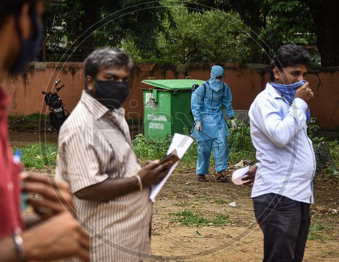 A Sanitary Worker Wearing Ppe Kit Arrives To Disinfect The Area As People Wait For The Covid-19 Test At Igmc Stadium, In Vijayawada, August 03, 2020.