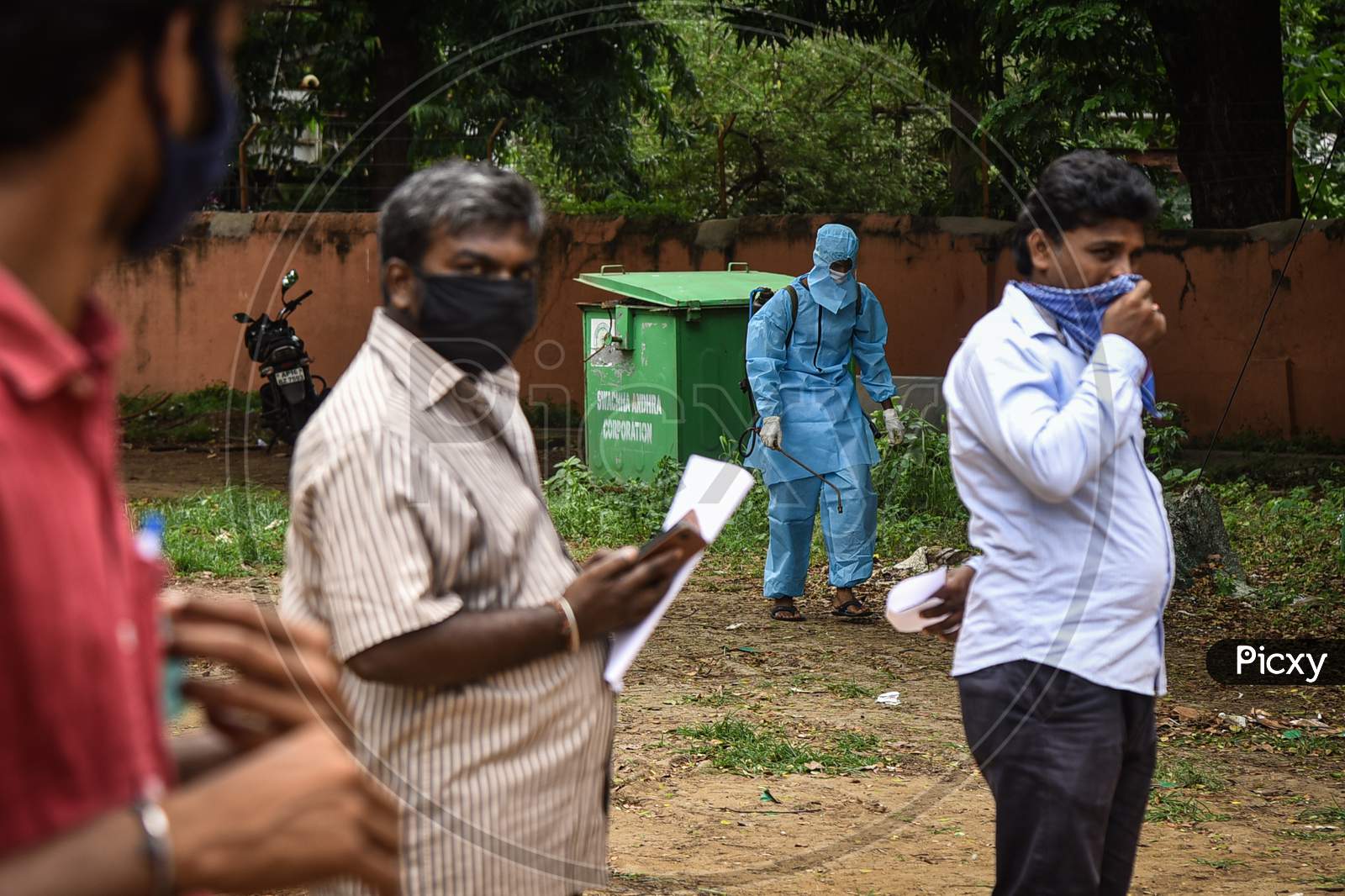 A Sanitary Worker Wearing Ppe Kit Arrives To Disinfect The Area As People Wait For The Covid-19 Test At Igmc Stadium, In Vijayawada, August 03, 2020.