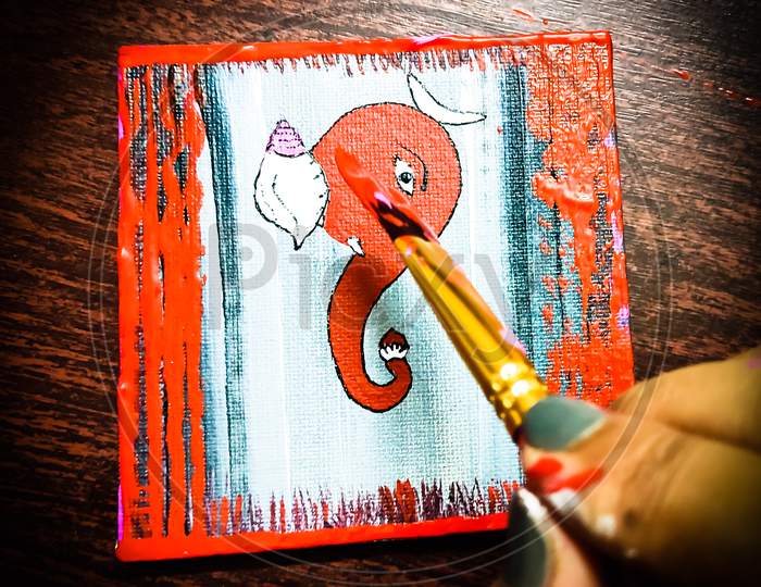 Painting a Lord Ganesha on a mini canvas with brush.