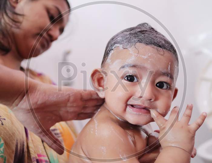 Indian Baby Enjoying Bubble Bath With Foam While Mother Rubs Soap On His Back