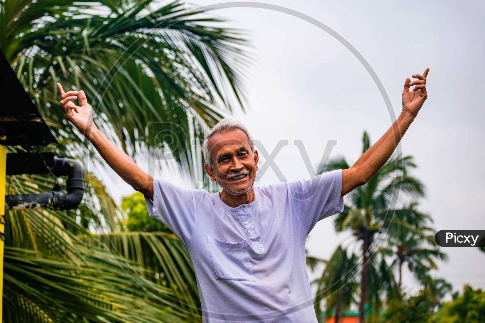 Close-up Portrait of Senior Man Doing Exercise. Happy alone old man, wearing white dress, giving pose with style and smiling at the camera. Elderly Man Is Enjoying Retirement In Nature In Afternoon.