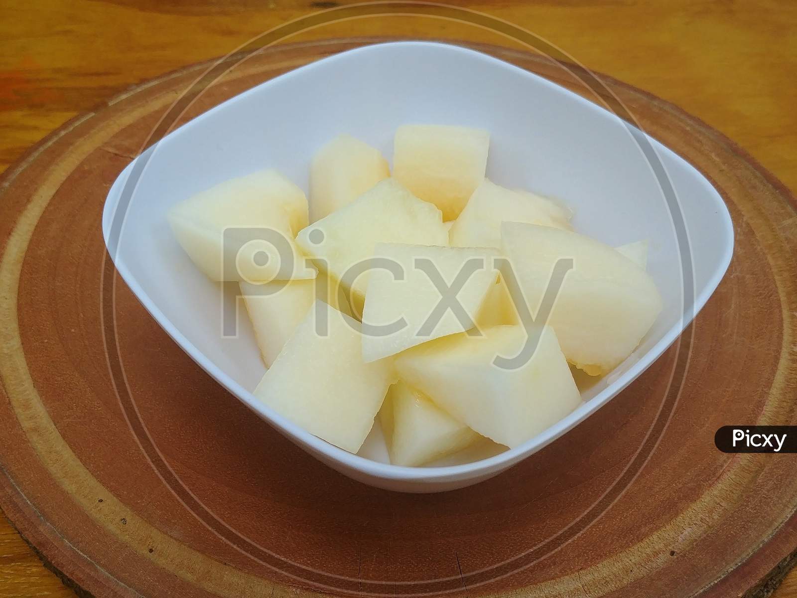 White melon cut into slices in a square bowl on a wooden base