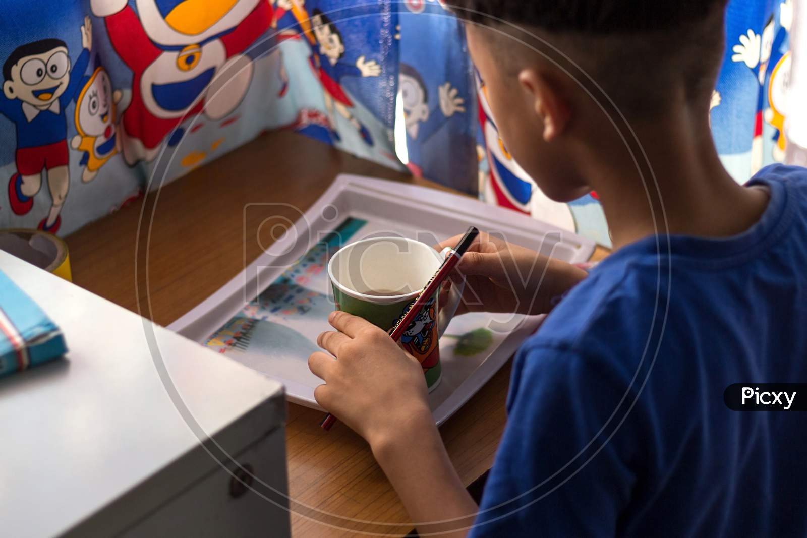 A Kid Having His Morning Breakfast Meal Of Chocolate Flavor Milk In A Cup.