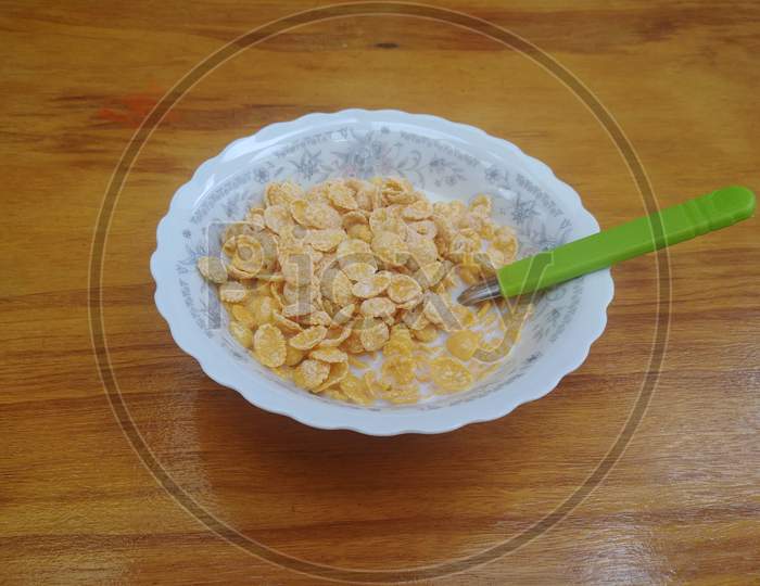 Breakfast with a cereal bowl with milk and a green spoon on the wooden table