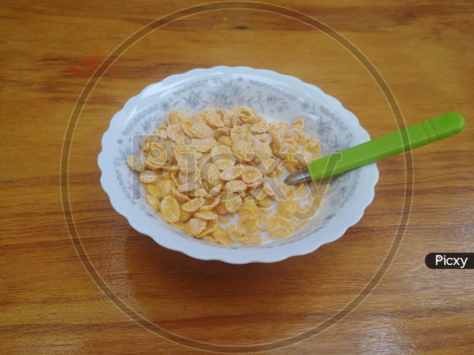 Breakfast with a cereal bowl with milk and a green spoon on the wooden table
