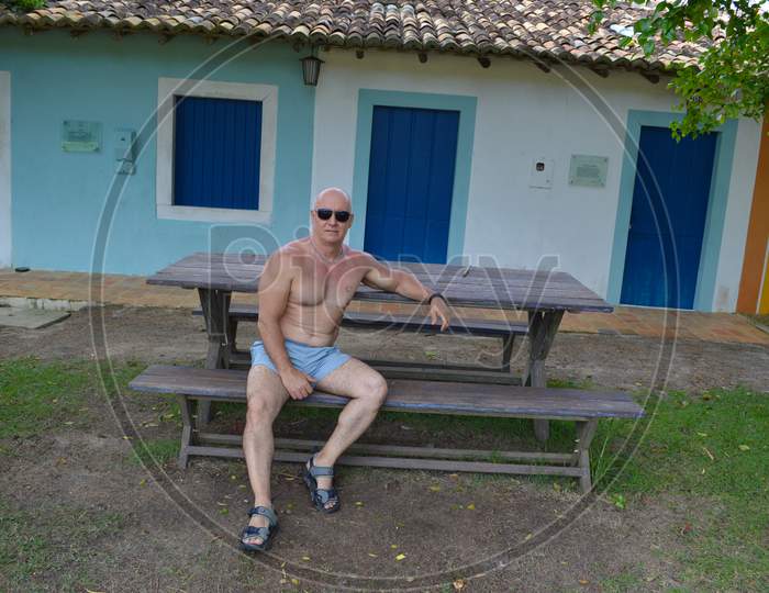 Mature and muscular man wearing sunglasses sitting on a bench in Trancoso