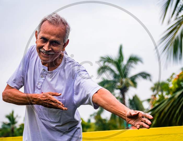 Close-up Portrait of Senior Man Doing Exercise. Happy alone old man, wearing white dress, giving pose with style and smiling at the camera. Elderly Man Is Enjoying Retirement In Nature In Afternoon.