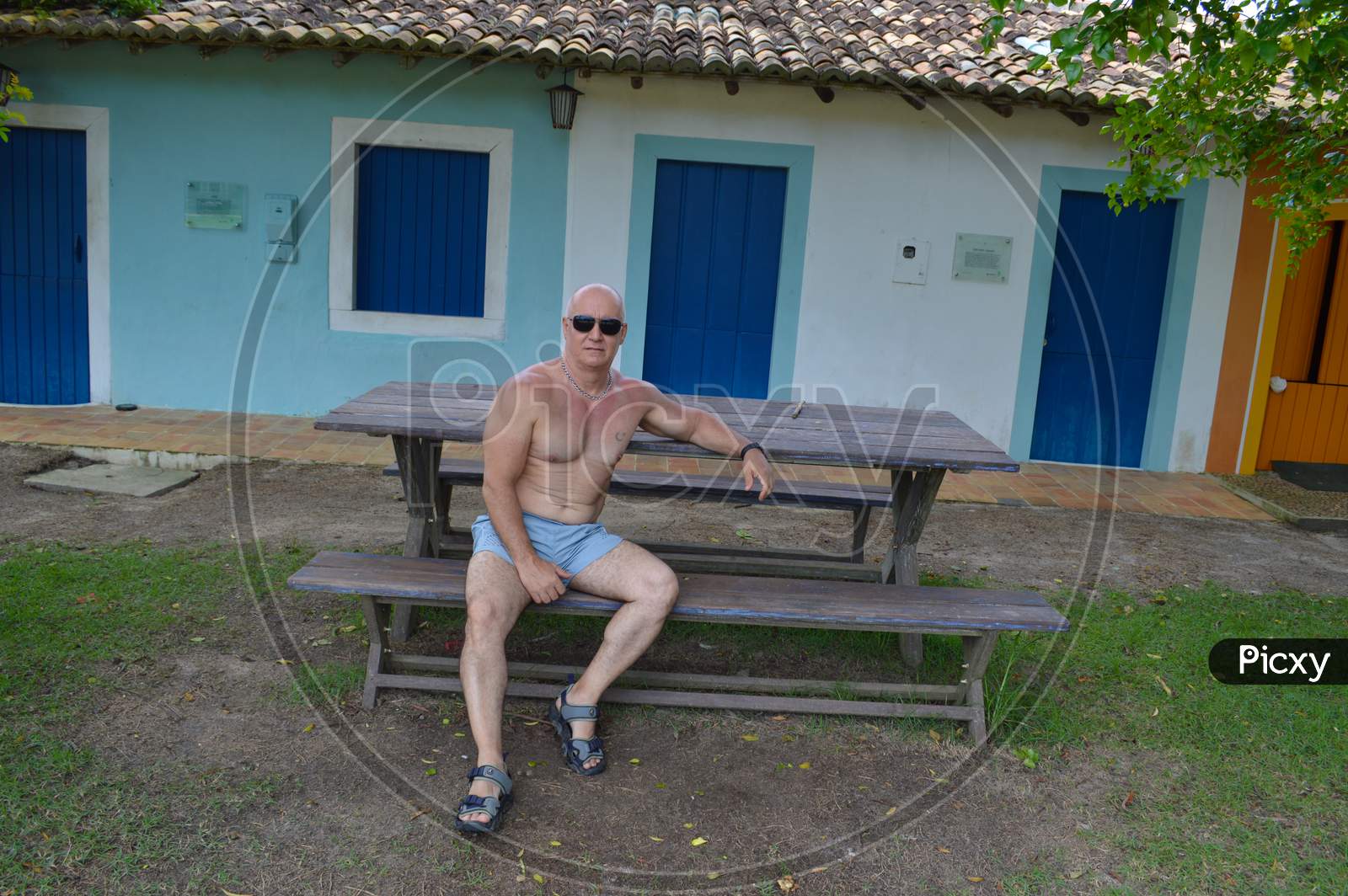 Mature and muscular man wearing sunglasses sitting on a bench in Trancoso