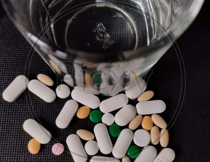 Close Up Of Medicine Tablets Or Pills And Water Glass Kept On Desk.