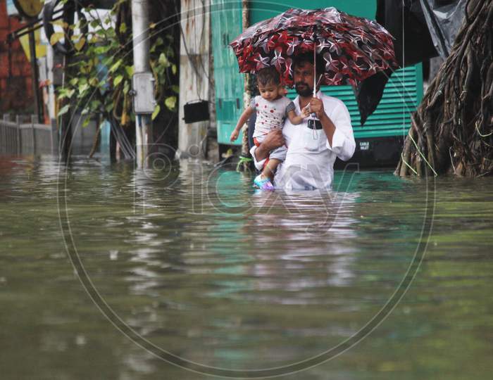 A man carries a kid in his hand and walks a waterlogged road during rains, in Mumbai, India on August 4, 2020.