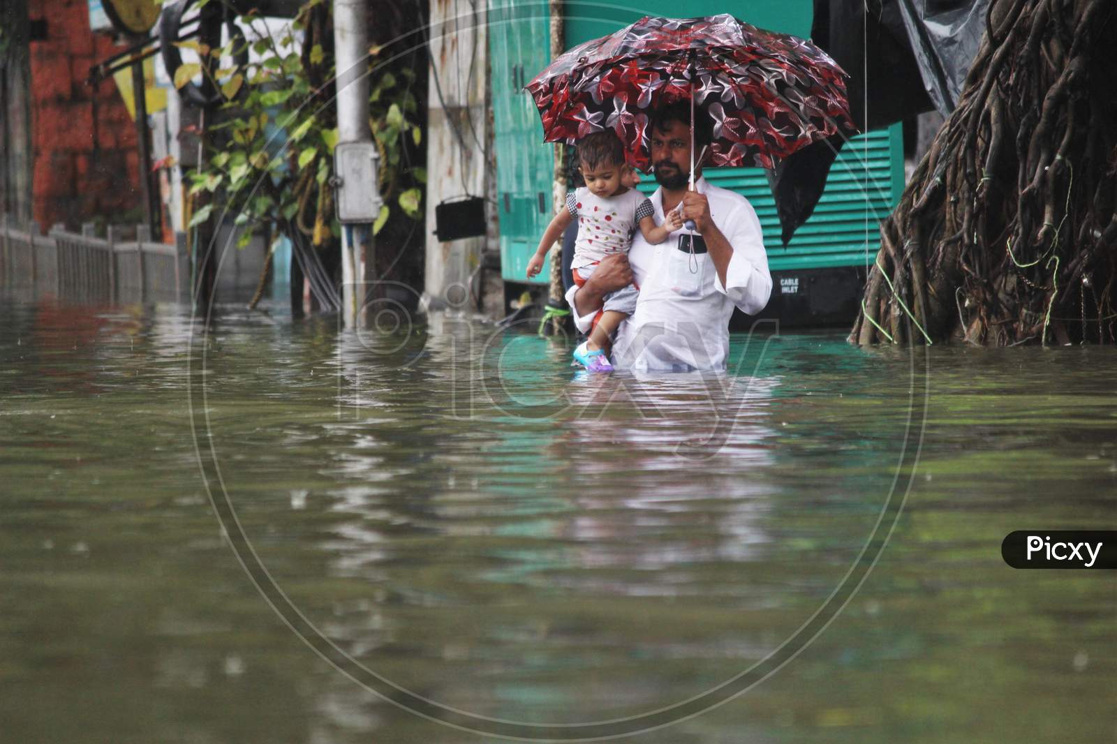 A man carries a kid in his hand and walks a waterlogged road during rains, in Mumbai, India on August 4, 2020.